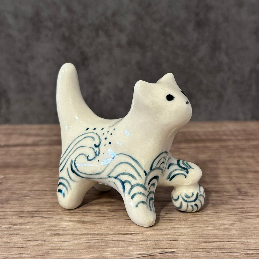 Hand made ceramic cat with a ball. Off White in color with dark blue waves design painted on.